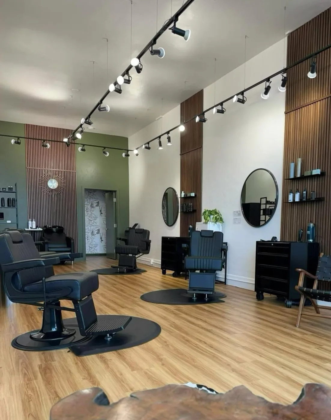 Inside Corte Madera Barbershop — black leather barber chairs on wood floors, round black-framed mirrors, slatted walnut accent walls and track lighting